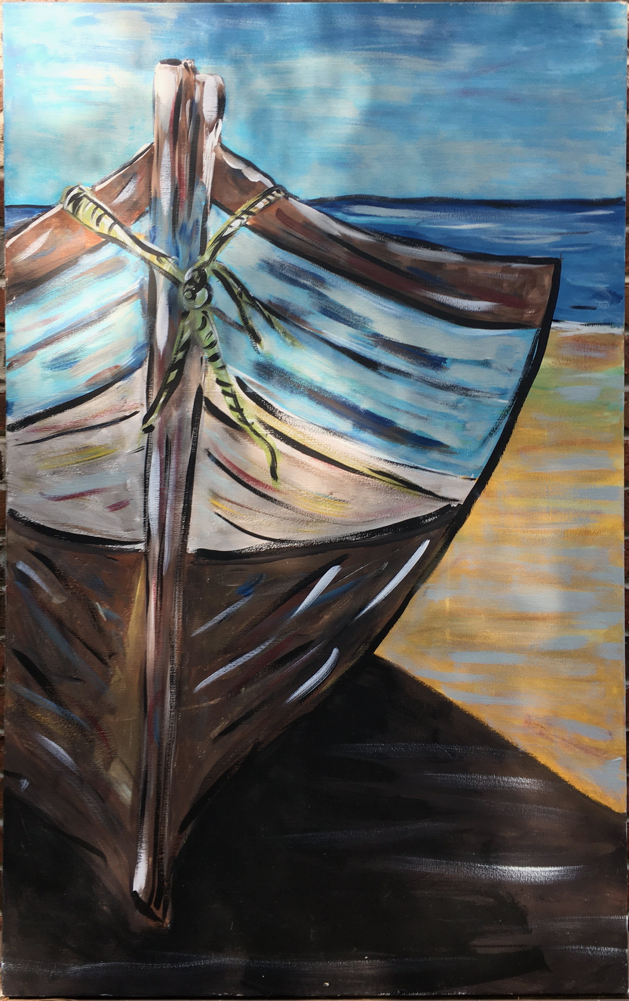 The bow of a wooden boat drawn up on ochre sand, dark hull below, blue sea and sky behind.