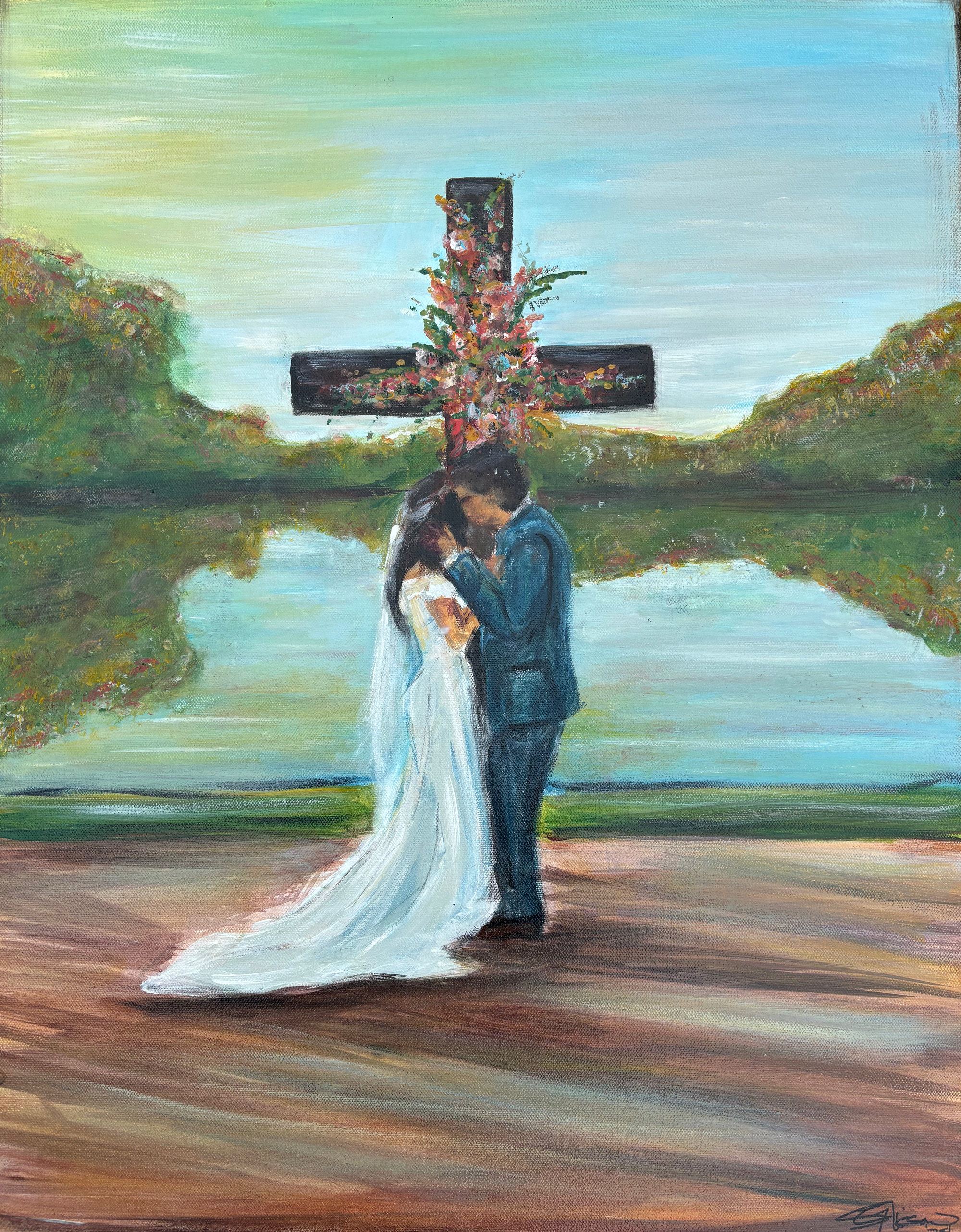 A bride and groom standing before a flowered cross at the edge of a lake, hills behind.